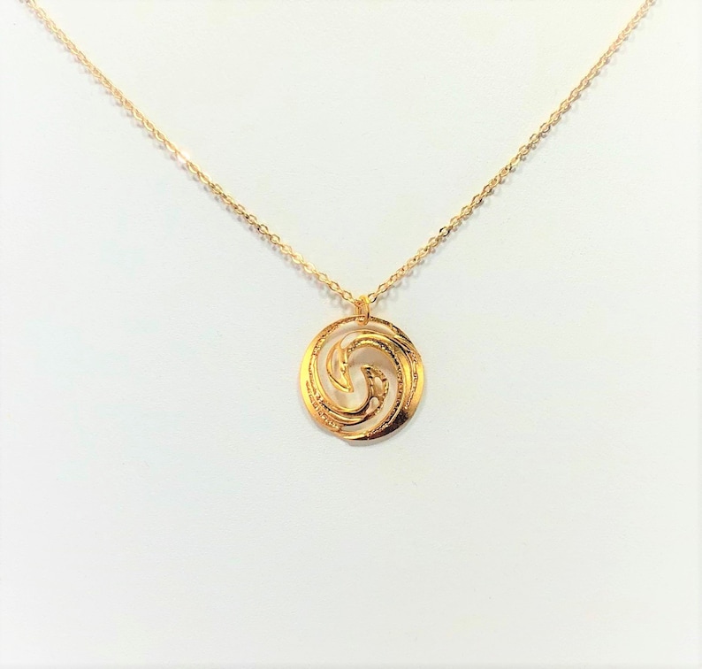 May include: A gold necklace with a circular pendant featuring a stylized wave design.