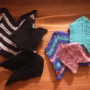 May include: A collection of hand-knitted items featuring pointed shapes. One set is black with white chevron stripes, while the other set includes solid turquoise, a pink piece, and a multi-colored blue, purple, and turquoise chevron-patterned piece.