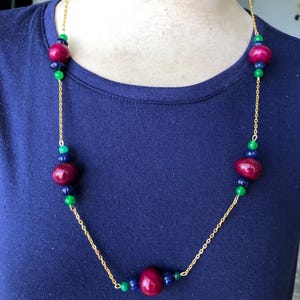 May include: A gold chain necklace with alternating dark red, dark green, and dark blue round beads.