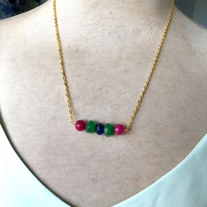 May include: A gold chain necklace with a row of five gemstone beads. The beads are green, blue, green, pink, and pink.