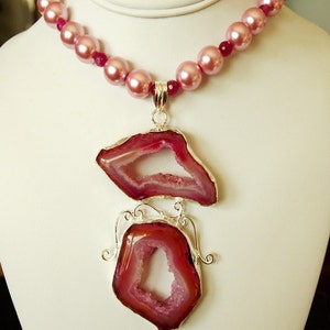 May include: A pink pearl necklace with a silver pendant featuring two pink agate slices with a crystal-like texture.