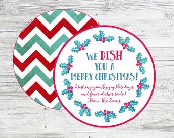 May include: A round Christmas gift tag with a red and green chevron pattern on the back. The front features a wreath of holly with red berries and the text "WE DISH YOU A MERRY CHRISTMAS! Wishing you Happy Holidays and fewer dishes to do! From, The Evans."