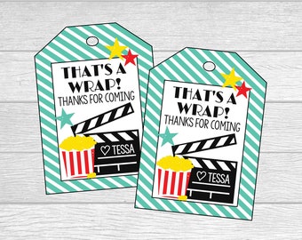 Könnte beinhalten: Zwei türkis-weiß gestreifte Geschenkanhänger mit einem Filmthema. Die Anhänger zeigen eine schwarz-weiße Filmklappe, einen rot-weißen Popcorn-Eimer und gelbe Sterne. Der Text auf den Anhängern lautet "That's a Wrap! Thanks for coming" und "Tessa".