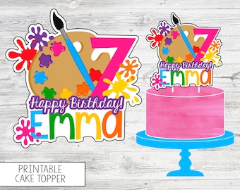 May include: A printable cake topper design featuring a pink number 7, a painter's palette with colorful paint splatters, and the text "Happy Birthday! Emma". The design includes a paintbrush and is suitable for a birthday celebration.