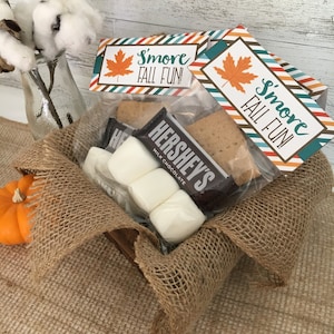 May include: A burlap gift bag filled with s'mores ingredients. The bag has a tag that says "S'more Fall Fun!" and includes graham crackers, Hershey's chocolate bars, and marshmallows.