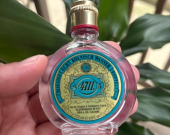Puede incluir: Una pequeña botella de vidrio transparente de colonia 4711. La botella tiene una tapa dorada y una etiqueta azul y dorada con el texto "Original Eau de Cologne 4711" y "Kölnsches Wasser" en alemán.