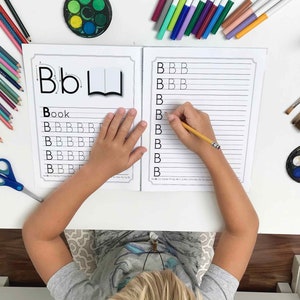 May include: A child practices writing the letter 'B' on a worksheet. The worksheet has a picture of a book and the word 'Book' written on it. The child is using a pencil to write the letter 'B' on the lines.