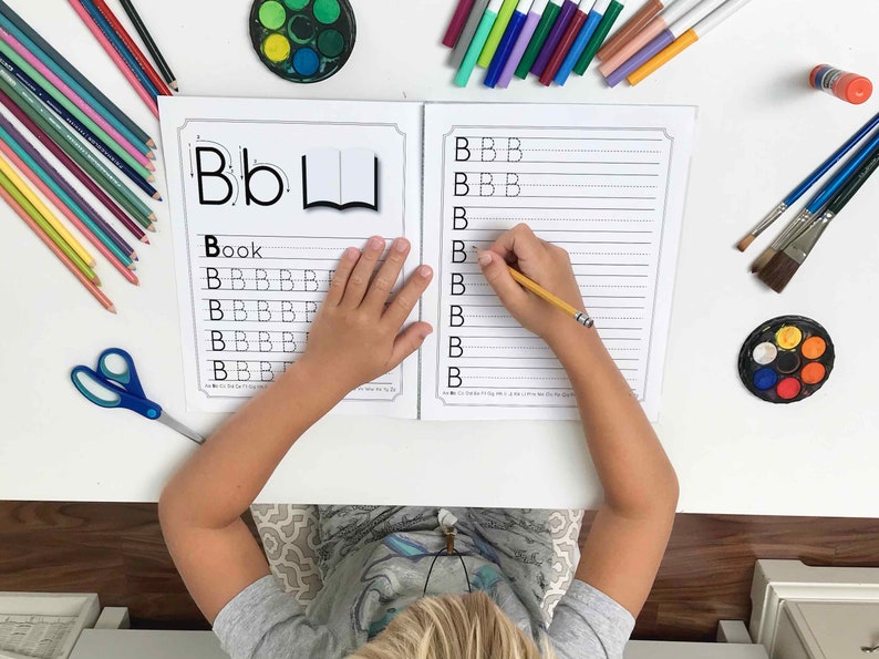 May include: A child practices writing the letter 'B' on a worksheet. The worksheet has a picture of a book and the word 'Book' written on it. The child is using a pencil to write the letter 'B' on the lines.