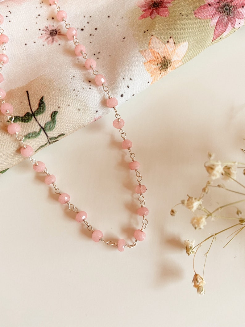 May include: A delicate pink beaded necklace with a silver chain. The beads are faceted and have a subtle shimmer.