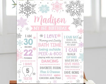 May include: A printable first birthday sign for a girl with a winter theme. The sign is white with silver and pink snowflakes. It says "Madison My 1st Birthday" and includes details like height, weight, and favorite foods.