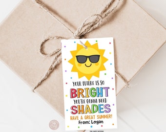 Op de afbeelding: Een wit cadeau-etiket met een cartoonzon die een zonnebril draagt. De tekst luidt "Je toekomst is zo helder dat je een zonnebril nodig hebt. Geniet van een fijne zomer! Van: Logan".