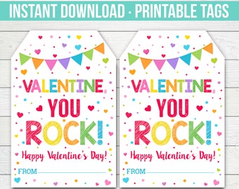 May include: Two printable Valentine's Day gift tags with a colorful design. The tags feature the text "Valentine, You Rock!" with a rainbow font and a heart border. The text "Happy Valentine's Day!" is printed below the main text. There is a blank line for the sender's name.