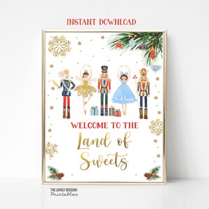 May include: A printable sign with a gold frame featuring a Nutcracker theme. The sign has a white background with gold snowflakes and stars. The text reads "Welcome to the Land of Sweets" in gold lettering. There are five Nutcracker characters, including a mouse king, a ballerina, and a soldier, all in colorful costumes.