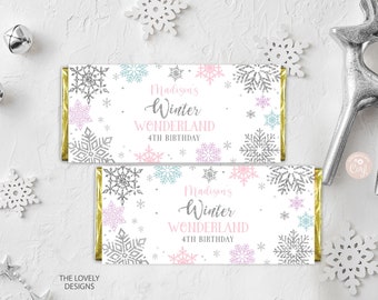 May include: Two white chocolate bar wrappers with a winter wonderland theme. The wrappers feature a snowflake pattern with pink, blue, and silver glitter accents. The text on the wrappers reads "Madison's Winter Wonderland 4th Birthday".