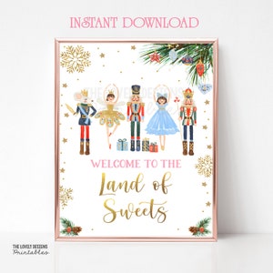 Puede incluir: Un cartel blanco imprimible con un marco dorado con temática de Cascanueces. El cartel tiene un mensaje de bienvenida rosa y dorado que dice "Bienvenido a la Tierra de los Dulces". El cartel presenta un ratón, una bailarina, un cascanueces y una princesa.