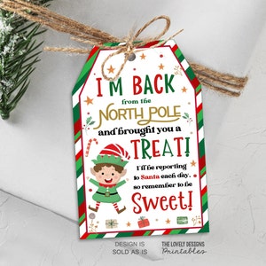 Puede incluir: Una etiqueta de regalo festiva con un borde rojo, verde y blanco, atada con hilo. La etiqueta presenta el texto "I'M BACK from the NORTH POLE and brought you a TREAT!" y una ilustración de un elfo.