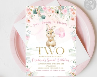 May include: A pink and white invitation card for a second birthday party. The card features a watercolor illustration of a bunny holding balloons, floral accents, and the text "some bunny is turning TWO". The invitation is on a pink plate.