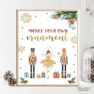 以下が含まれることがあります： 「あなただけのオーナメントを作ろう」という金と赤の文字が書かれた白い印刷可能なサイン。サインには、ナッツクラッカー、バレリーナ、そしてオーナメントで飾られたクリスマスツリーが描かれている。背景は、金色の星と雪片が散りばめられた白である。