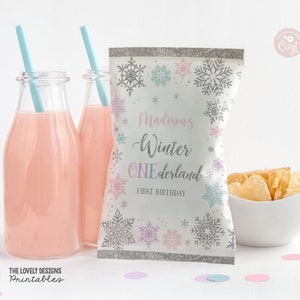 May include: A white favor bag with a silver glitter border and snowflake designs in pink, blue, and silver. The bag has the text "Madison's Winter Wonderland First Birthday" printed on it.