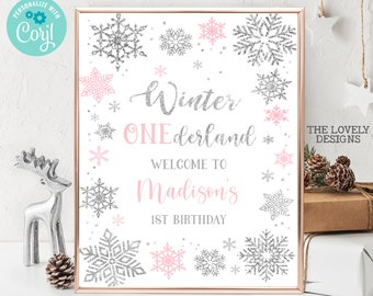 May include: A white sign with a silver glitter border and snowflakes. The text on the sign reads "Winter Wonderland, Welcome to Madison's 1st Birthday".