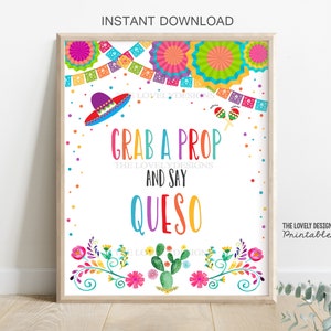 May include: A printable sign with a white background and colorful decorations. The text reads "Grab a prop and say Queso." The sign is decorated with colorful flowers, cacti, and a sombrero.
