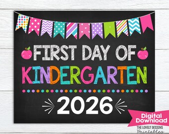 May include: A chalkboard-style sign featuring a colorful bunting banner at the top, two pink apple illustrations, and the text FIRST DAY OF KINDERGARTEN in multi-colored letters. The year 2026 is printed in large white font at the bottom center.
