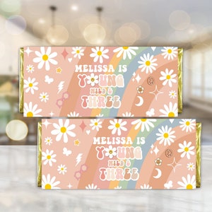 May include: Two printable chocolate bar wrappers with a pink and white daisy pattern. The wrappers feature a rainbow and the text "Melissa is turning wild & three".