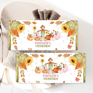 May include: Two candy bar wrappers with a fall theme. Each wrapper features a scarecrow, pumpkins, sunflowers, and fall leaves. The text "MADISON'S 4TH BIRTHDAY" is displayed in pink. The wrappers are decorated with gold foil.