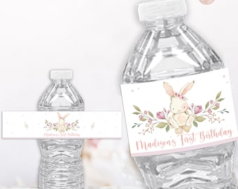 May include: Clear plastic water bottles with custom labels. The labels feature a watercolor illustration of a bunny with a floral crown and the text "Madison's First Birthday" in pink script. The Lovely Designs Printables logo is visible.