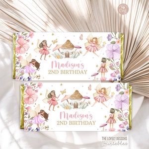 Pode incluir: Duas embalagens de barras de chocolate com tema de fadas. As embalagens apresentam ilustrações de fadas, flores, cogumelos e o texto "Madison's 2nd Birthday". O design inclui detalhes em rosa, roxo e dourado.