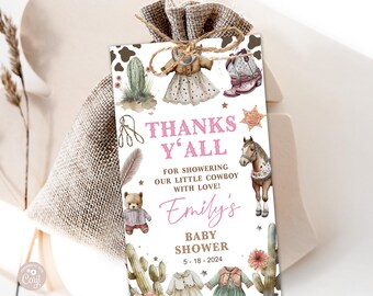 May include: A pink and brown thank you tag with a cowboy theme. It says "Thanks Y'all" for showering our little cowboy with love! Emily's Baby Shower 5-18-2024. The tag features a cactus, a horse, a teddy bear, and a cowboy hat.
