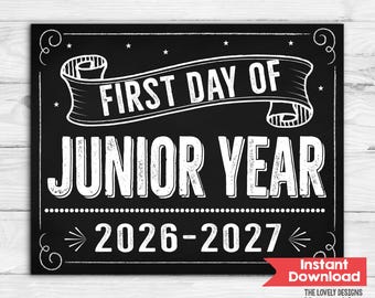 May include: A black rectangular sign with white text and decorative borders. The text reads FIRST DAY OF JUNIOR YEAR 2026-2027. The design features a banner graphic across the top and small stars scattered throughout the chalkboard-style background.