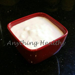 Puede incluir: Primer plano de un bol cuadrado rojo lleno de yogur blanco. El bol está sobre una superficie negra.