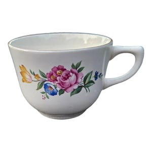 May include: White teacup with a floral design featuring pink roses, blue and yellow flowers, and green leaves. The teacup has a curved handle and a gold rim. A classic piece for tea or coffee.
