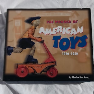 May include: The Wonder of American Toys book cover features a cartoon illustration of a child riding a red "Smitty Scooter" toy. The book title is in blue and red lettering with the years 1920-1950 below. The author, Charles Dee Sharp, is credited at the bottom.