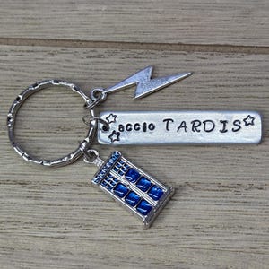 Puede incluir: Un llavero de metal plateado que incluye una anilla circular, un dije de rayo, una placa rectangular grabada con el texto accio TARDIS y estrellas, y un dije de cabina de policía en tonos azul y plateado.