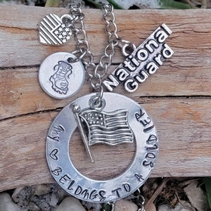 May include: Silver necklace with a charm that says "My heart belongs to a soldier" and another charm that says "National Guard". The necklace also has a small American flag charm and a boot charm.