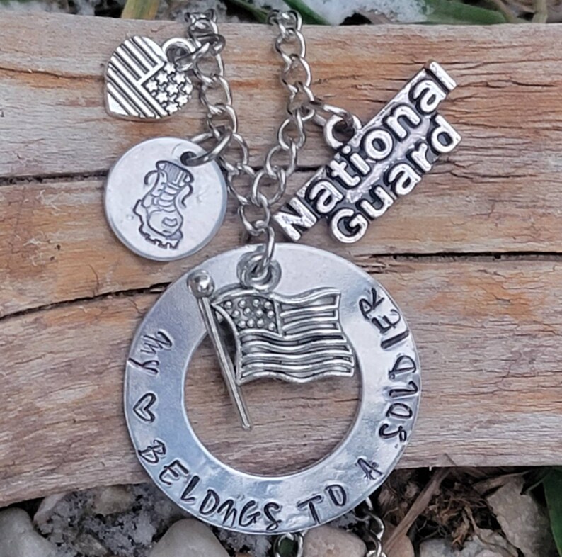 May include: Silver necklace with a charm that says "My heart belongs to a soldier" and another charm that says "National Guard". The necklace also has a small American flag charm and a boot charm.