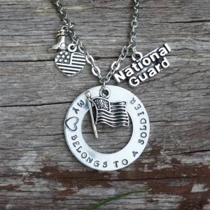 May include: Silver necklace with a heart charm that says "I am a soldier", a circle charm that says "My heart belongs to a soldier", a small American flag charm, and a charm that says "National Guard".