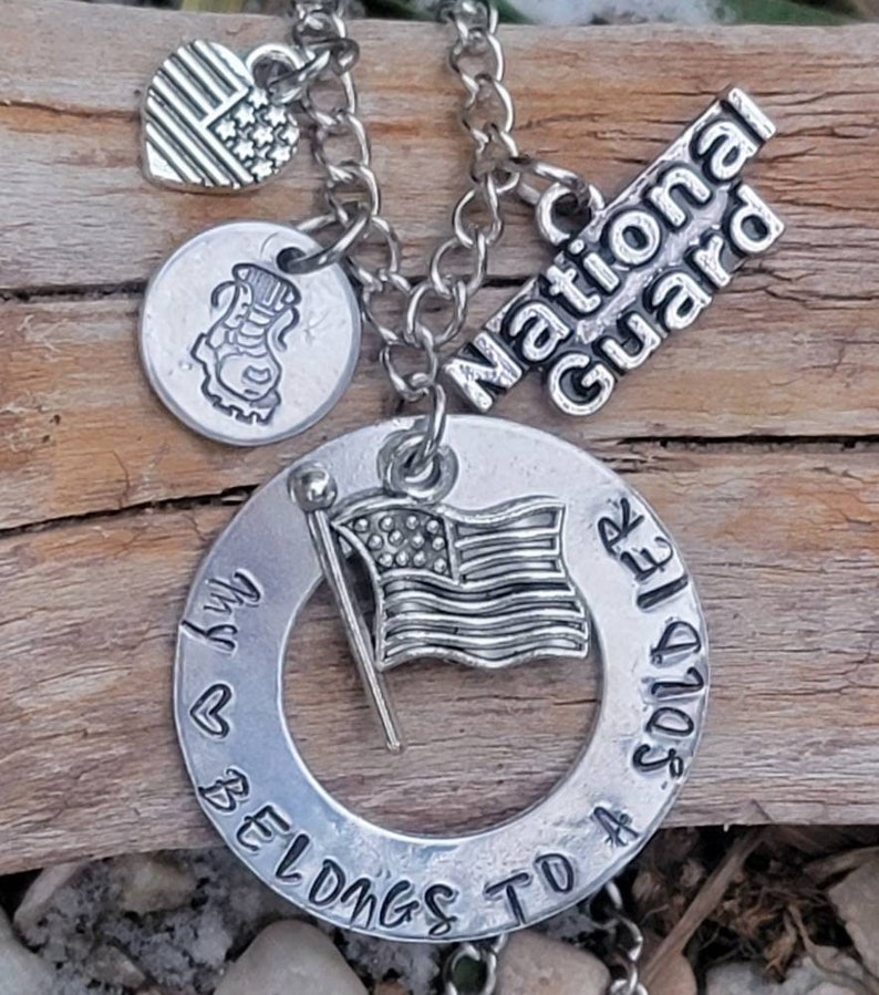 May include: Silver necklace with charms, including a heart with an American flag, a boot, a flag, and a circle charm that says "My heart belongs to a soldier". The charm with the flag also says "National Guard".