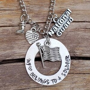 May include: Silver necklace with a charm that says "My heart belongs to a soldier" and another charm that says "National Guard". The necklace also has a small American flag charm and a boot charm.