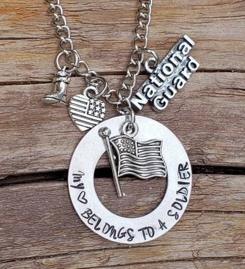 May include: Silver necklace with a charm that says "My heart belongs to a soldier" and another charm that says "National Guard". The necklace also has a small American flag charm and a boot charm.