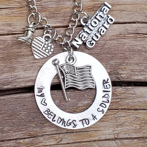 May include: Silver necklace with a charm that says "My heart belongs to a soldier" with a small American flag, boot, and a charm that says "National Guard".