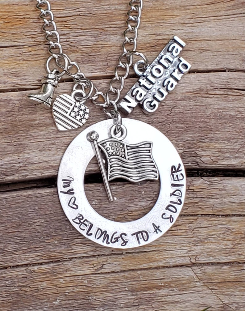May include: Silver necklace with a charm that says "My heart belongs to a soldier" with a small American flag, boot, and a charm that says "National Guard".