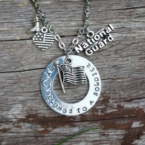 May include: Silver necklace with a heart charm that says "My heart belongs to a soldier" and a charm that says "National Guard". The necklace also has a small American flag charm.