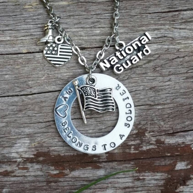 May include: Silver necklace with a heart charm that says "My heart belongs to a soldier" and a charm that says "National Guard". The necklace also has a small American flag charm.