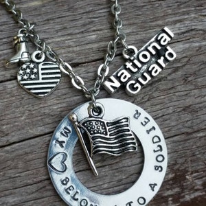 May include: A silver necklace with a charm that says "My heart belongs to a soldier" with a small American flag charm. The necklace also has a charm that says "National Guard" and a small heart charm with stars.
