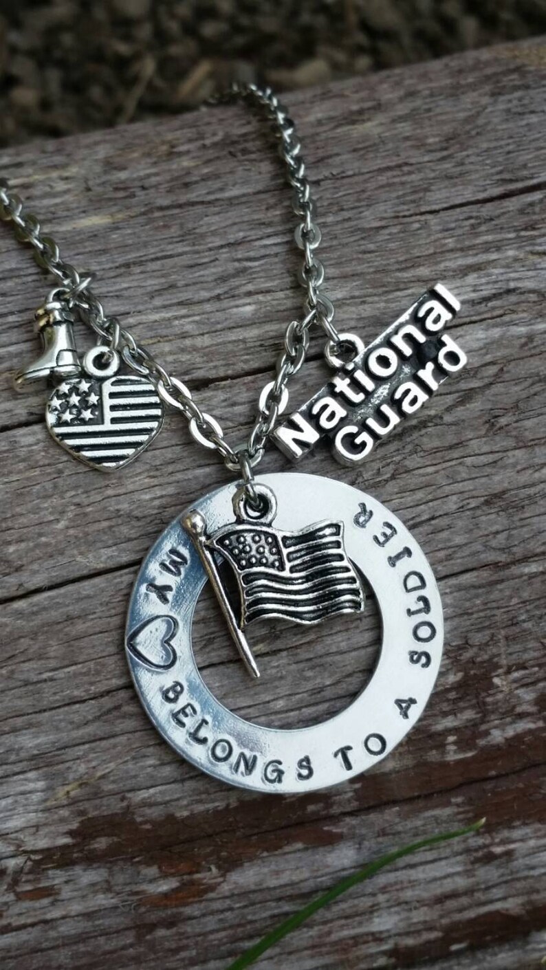 May include: A silver necklace with a charm that says "My heart belongs to a soldier" with a small American flag charm. The necklace also has a charm that says "National Guard" and a small heart charm with stars.