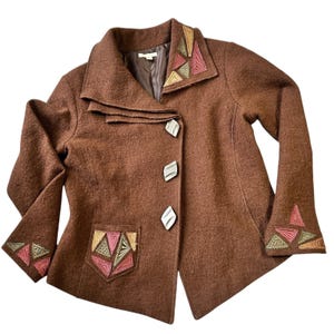 May include: A brown wool jacket with decorative geometric embroidery in pink, green, and gold on the collar, cuffs, and pocket. The jacket features three decorative buttons and a unique collar design.