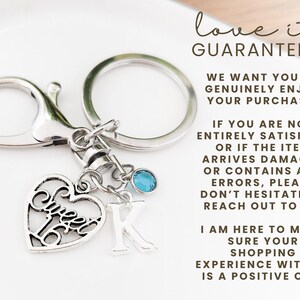 May include: Silver-toned keychain with a heart-shaped charm that says "Sweet 16". The keychain also includes a letter "K" charm and a small blue gemstone. The keychain is attached to a clasp and a key ring.